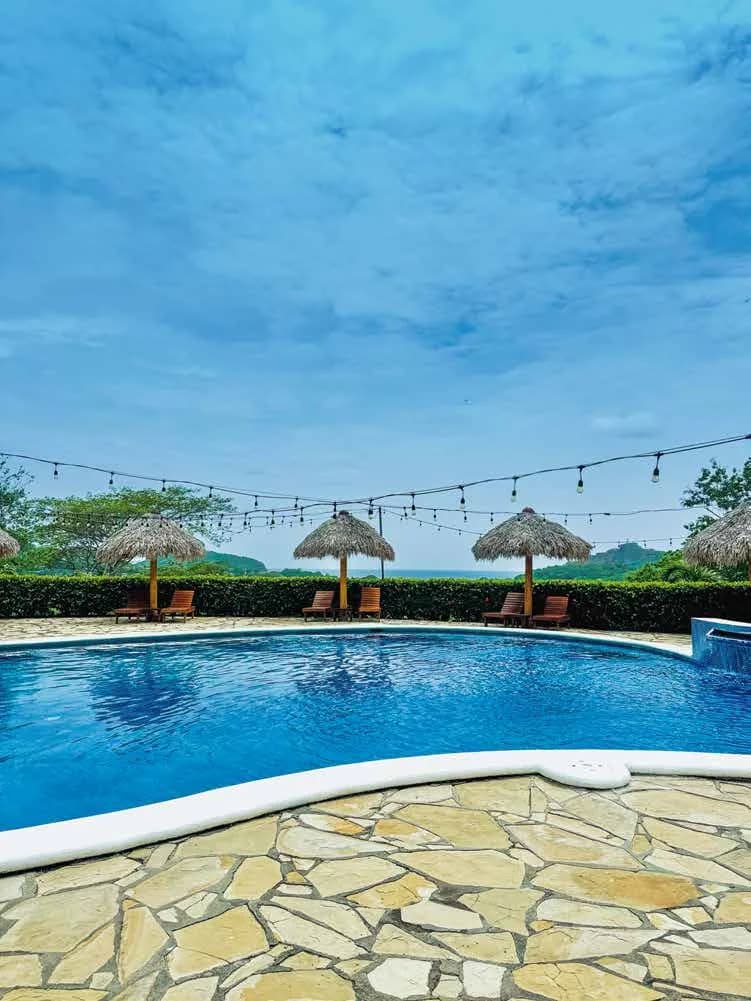 The pool, palapa umbrellas and loungers with the ocean on the horizon