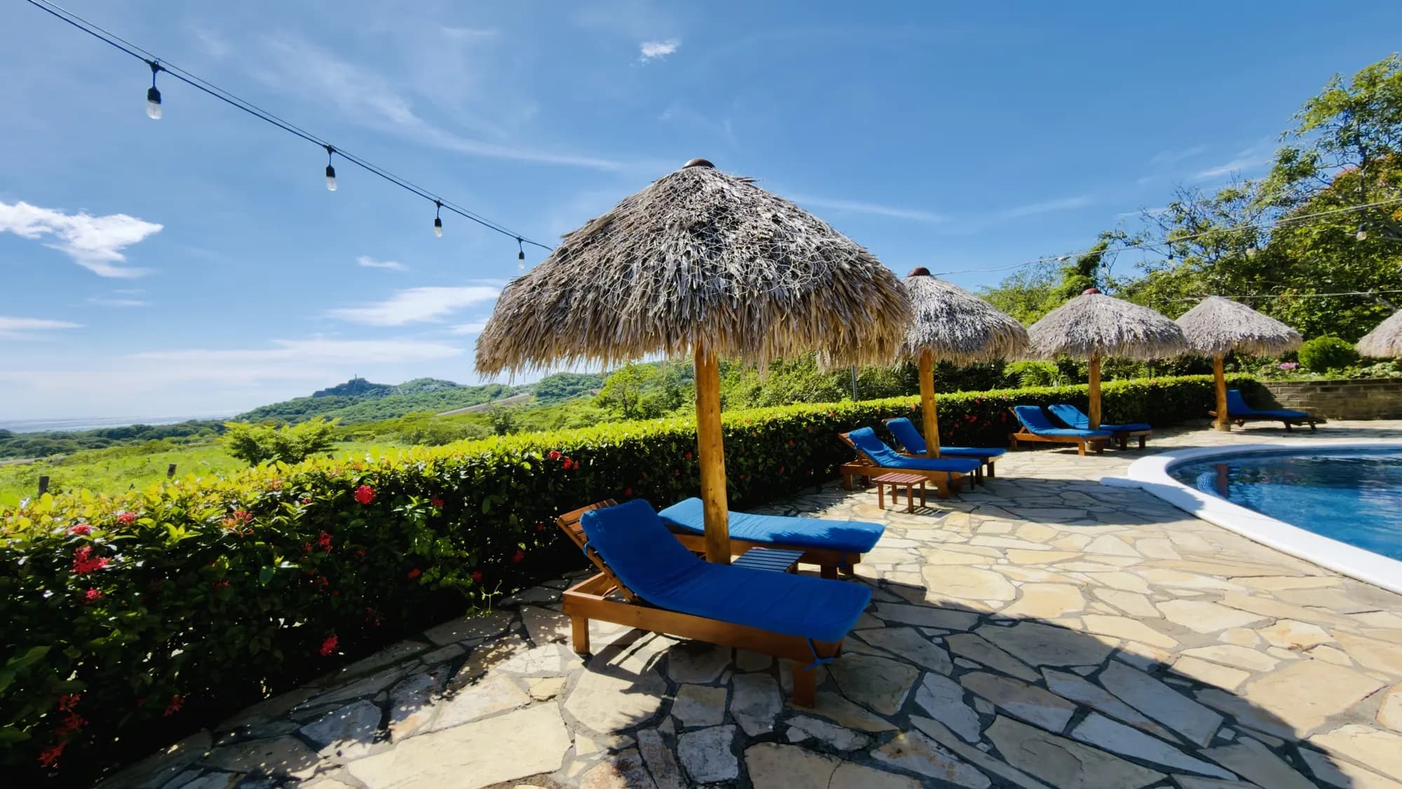A palm-thatch umbrella and loungers by the pool, hills beyond