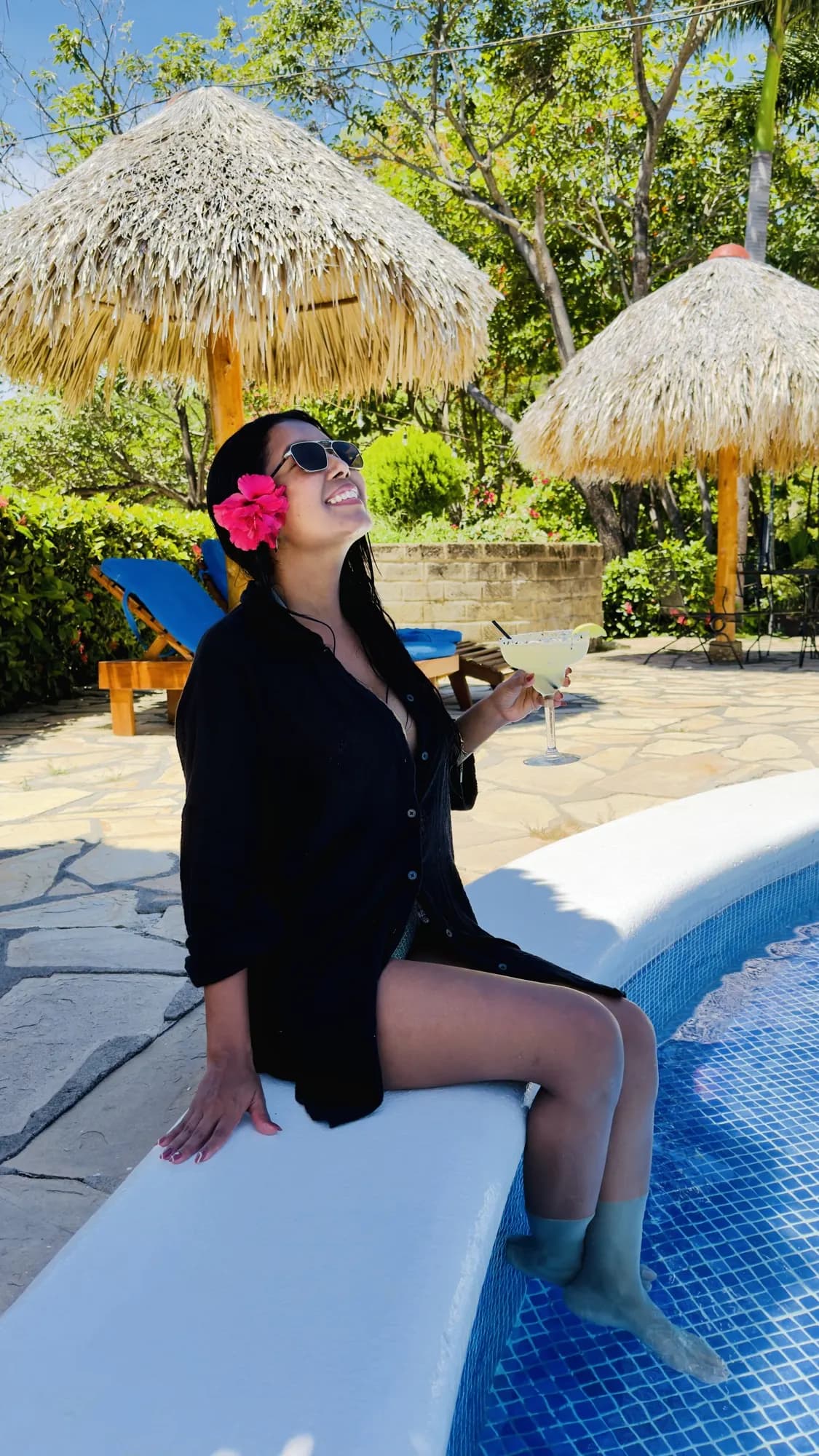 A guest with a cocktail on the pool's edge under the palapas